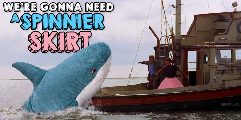 A scene from the movie Jaws showing the shark attacking the boat, but Jaws has been replaced by the IKEA stuffed toyy Blahaj and ROy Scheider is showing wearing a pink skirt.  The caption says "We're gonna need a spinnier skirt."